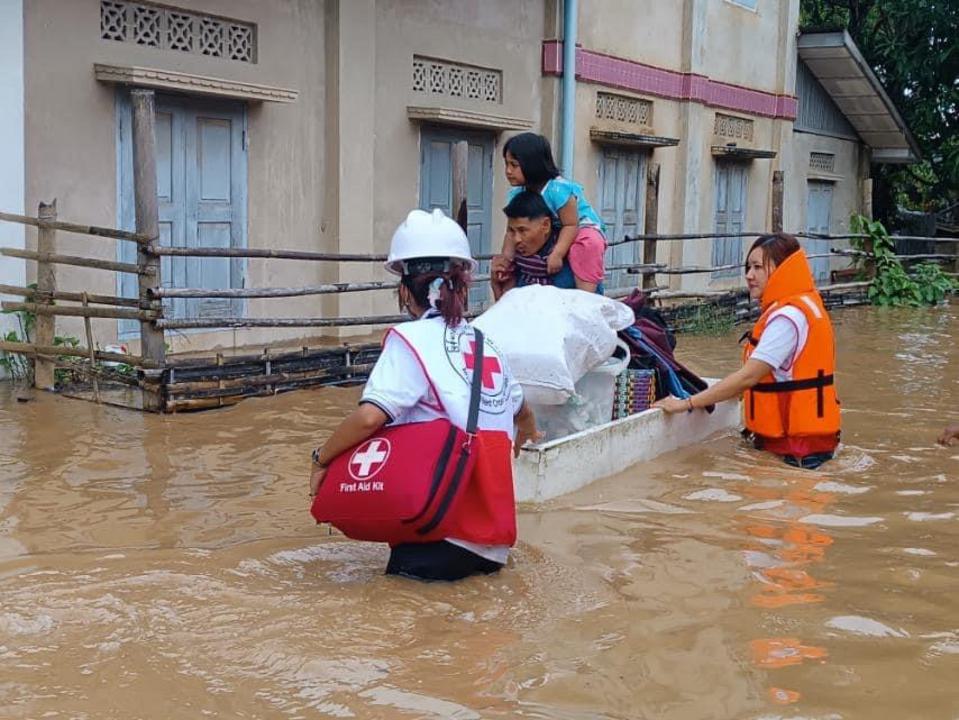 Civilian Myanmar Red Cross volunteers evacuate a family and belongings through a flooded neighbourhood.